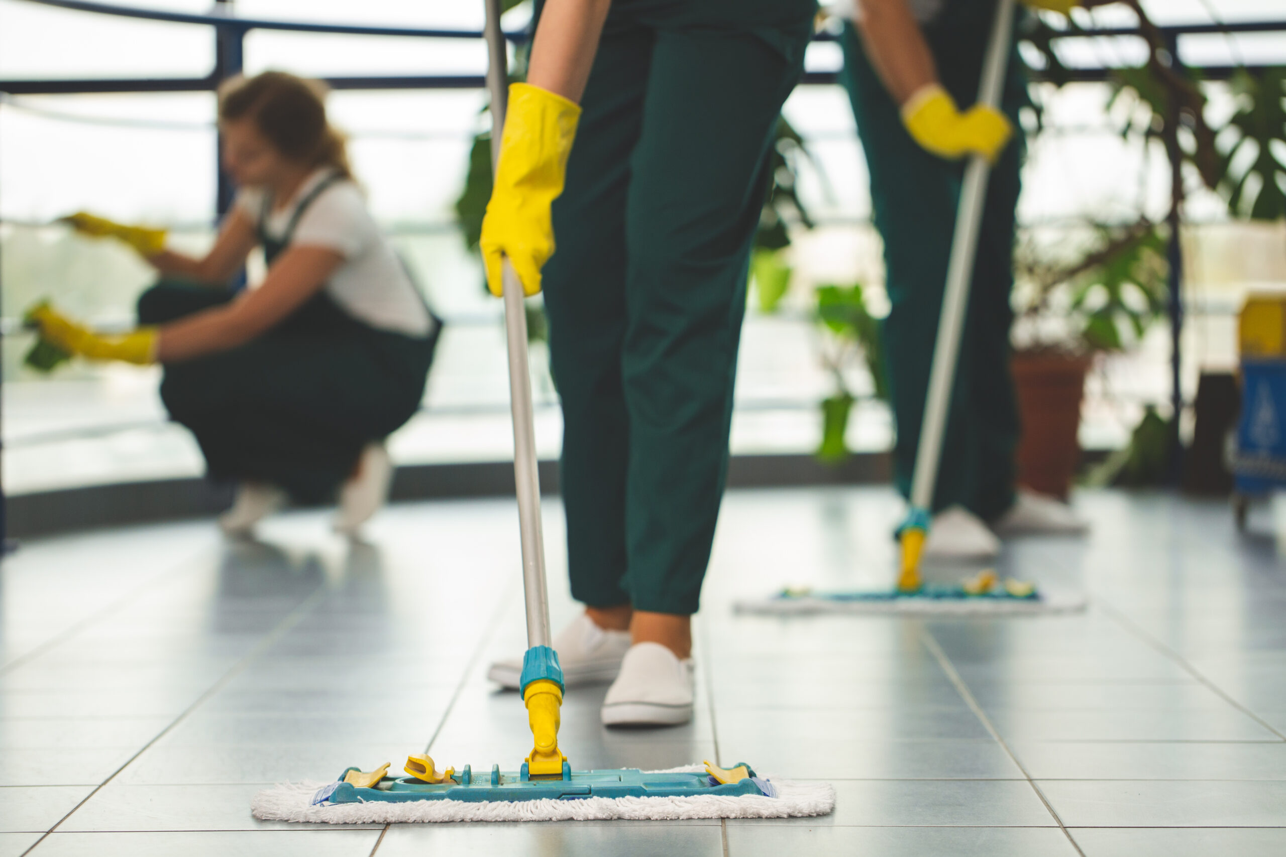 Close-up on cleaning specialist with yellow gloves holding mop while wiping floor Close-up on cleaning specialist with yellow gloves holding mop while wiping floor