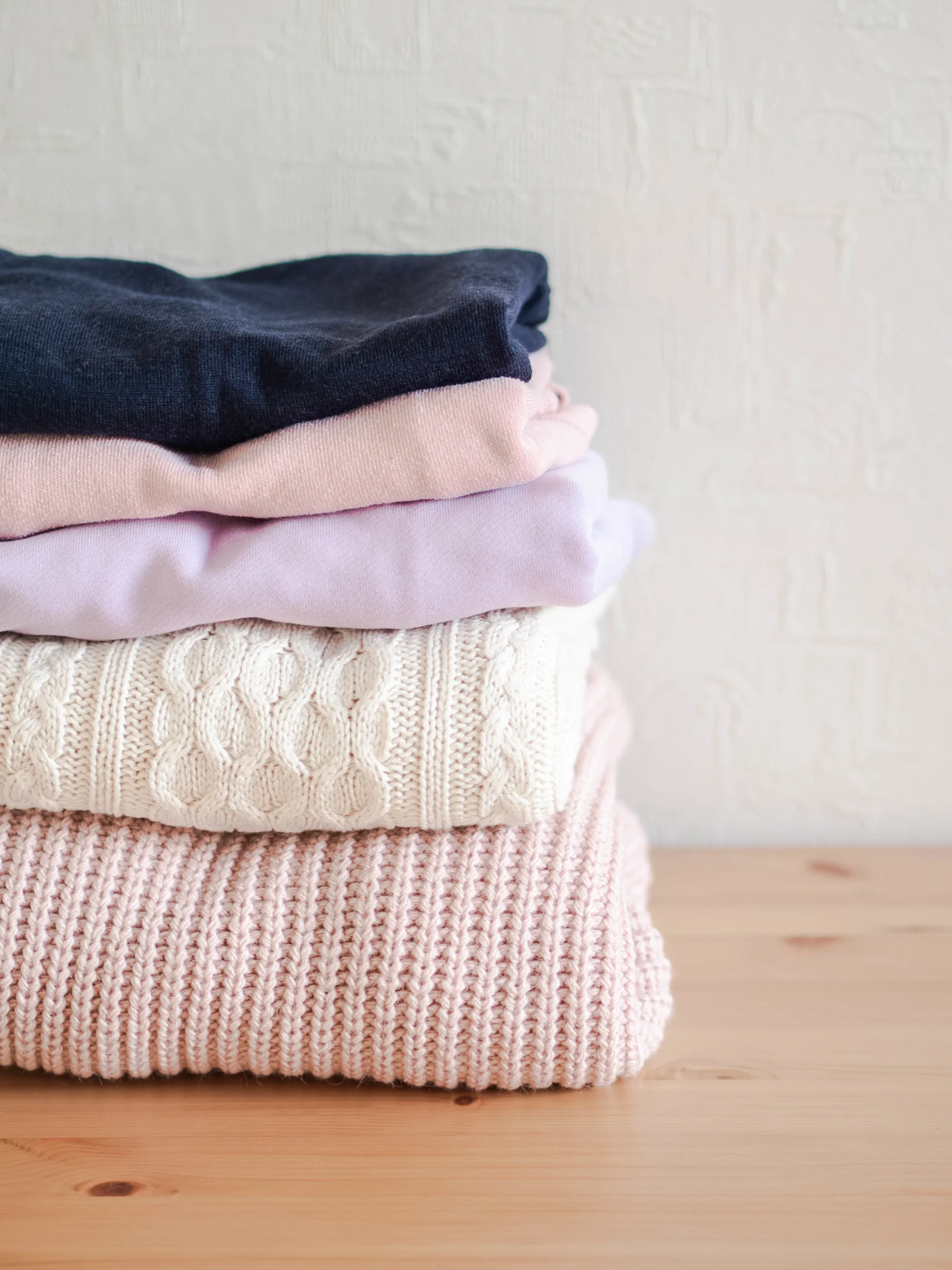 136049051_l (2) Stack of warm knitted woolen sweaters pastel shades and dark blue on a wood table